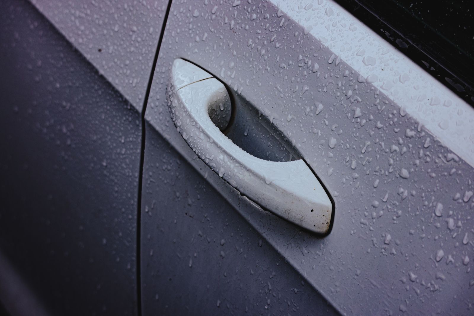 車門把手與車門表面布滿雨滴的細節特寫，代表入秋檢查汽車膠條與天窗排水孔的防水主題