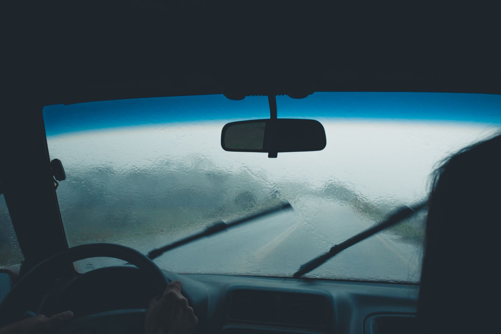 雨天從駕駛座看出去的車內視角，水珠布滿前擋風玻璃，雨刷正在作動，代表車內玻璃起霧與除霧主題