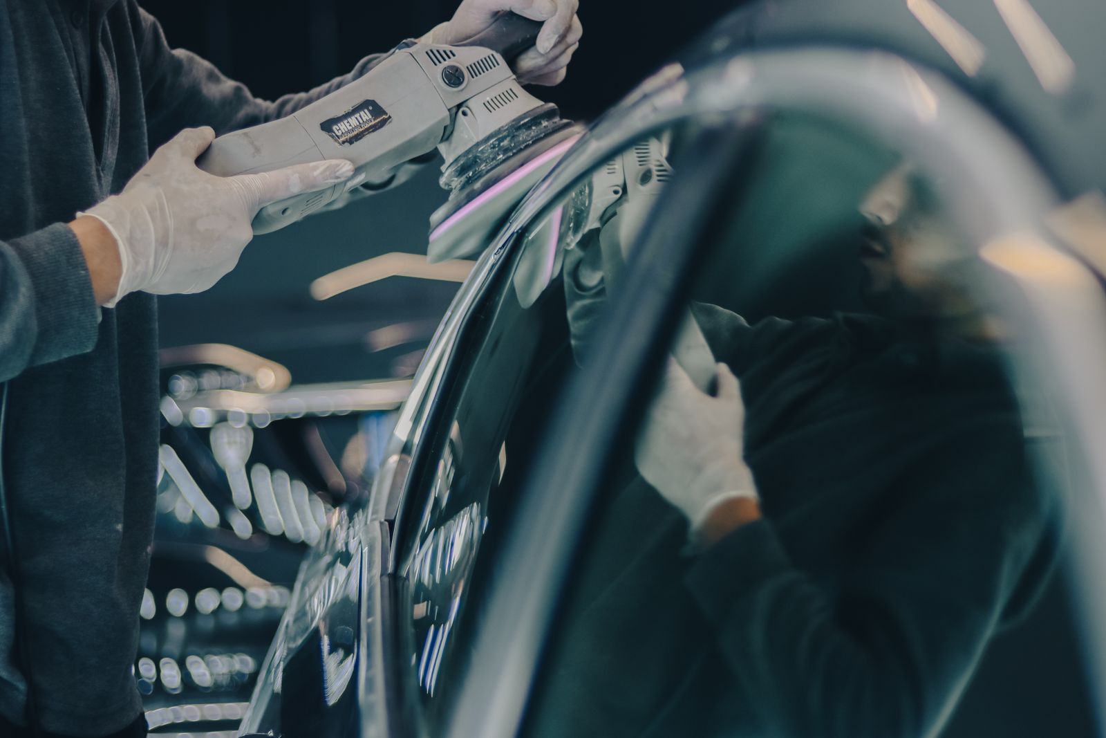 戴手套的施工人員使用汽車美容拋光機處理光亮車身表面的特寫